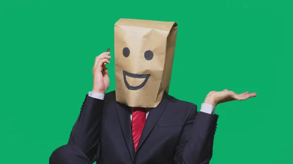 Concepto de emociones, gestos. un hombre con bolsas de papel en la cabeza, con un emoticono pintado, sonrisa, alegría. hablando por un teléfono celular — Foto de Stock