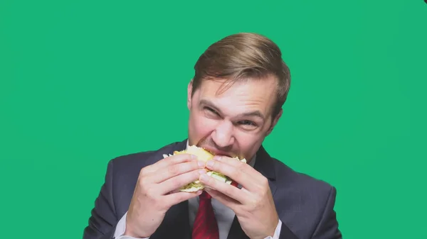 นักธุรกิจกินแซนวิชบนพื้นหลังสีเขียว แนวคิดมื้อเที่ยงอย่างรวดเร็ว — ภาพถ่ายสต็อก