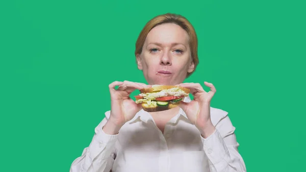 Donna d'affari mangiare un panino su uno sfondo verde. concetto di pranzo veloce . — Foto Stock