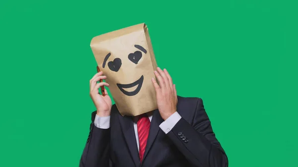 Concept van emoties, gebaren. een man met papieren zakken op zijn hoofd, met een geschilderde emoticon, glimlach, vreugde, liefde. praten op een mobiele telefoon — Stockfoto