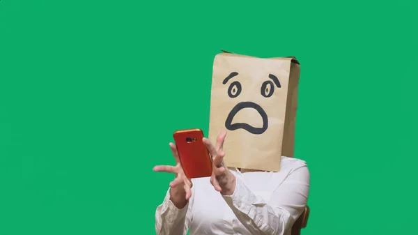 Concepto de emociones, gestos. un hombre con bolsas de papel en la cabeza, con un emoticono pintado, miedo. hablando por un teléfono celular — Foto de Stock