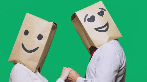 Concepto de emociones, gestos. un par de personas con bolsas de papel en la cabeza, con un emoticono pintado, sonrisa, alegría, ojos enamorados . — Foto de Stock