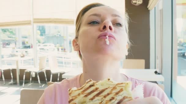 Mooie vrouw een broodje eten en drinken koffie in een café fastfood. fastfood. — Stockvideo