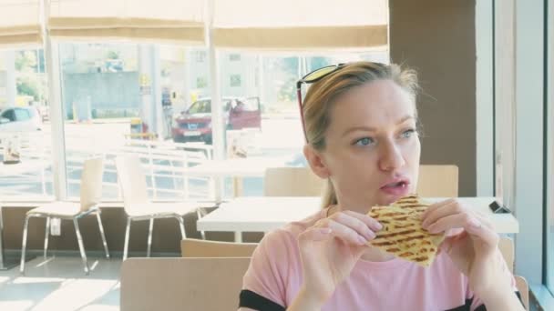 Una mujer guapa comiendo un sándwich y tomando café en un café de comida rápida. comida rápida . — Vídeo de stock