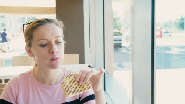 Szép nő, enni egy szendvicset, és kávét iszik egy gyorsétterem kávézóban. gyorsétterem. — Stock videók