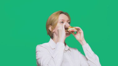 iş kadını yeşil bir arka plan üzerinde bir sandviç yeme. Hızlı öğle yemeği kavramı.
