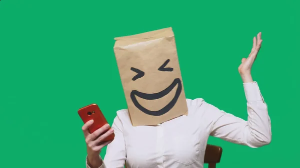 Concepto de emociones, gestos. un hombre con bolsas de papel en la cabeza, con un emoticono pintado, sonrisa, alegría. hablando por un teléfono celular — Foto de Stock