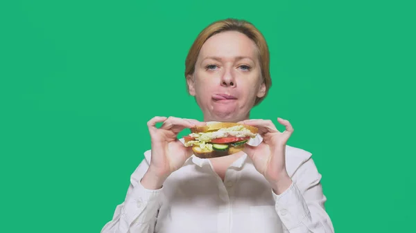 Mulher de negócios comendo uma sanduíche em um fundo verde. conceito de almoço rápido . — Fotografia de Stock