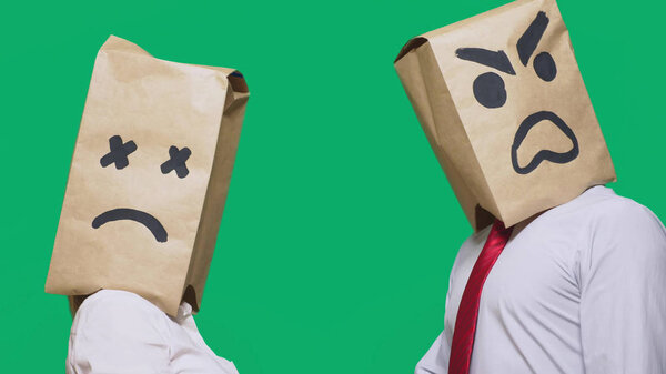 The concept of emotions and gestures. Two people in paper bags with smileys. Aggressive smiley swears. The second listens to him wearily