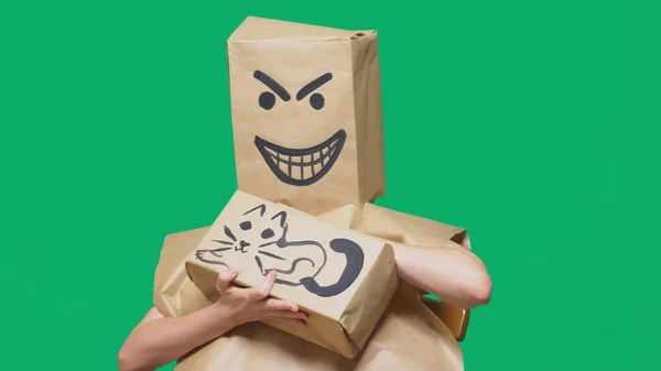 Concepto de emoción, gestos. un hombre con un paquete en la cabeza, con una sonrisa pintada enojado, astuto, regodeando y acariciando a un gato pintado en una caja . — Foto de Stock
