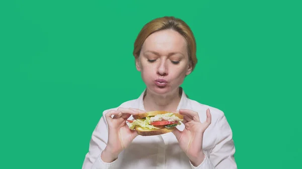 Mulher de negócios comendo uma sanduíche em um fundo verde. conceito de almoço rápido . — Fotografia de Stock