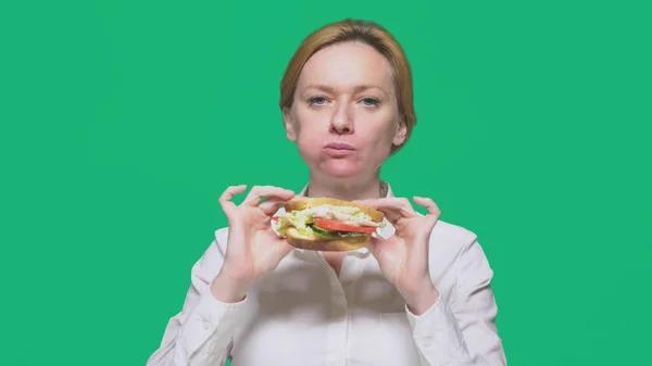Affärskvinna som äter en smörgås på en grön bakgrund. snabb lunch koncept. — Stockfoto