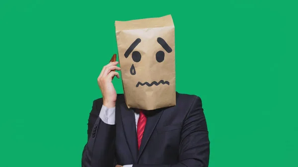 Концепция эмоций, жестов. мужчина с пакетом на голове, с нарисованной надписью плачет, грустит, разговаривает по телефону — стоковое фото