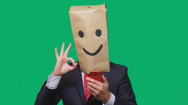 Concepto de emociones, gestos. un hombre con bolsas de papel en la cabeza, con un emoticono pintado, sonrisa, alegría. hablando por un teléfono celular —  Fotos de Stock