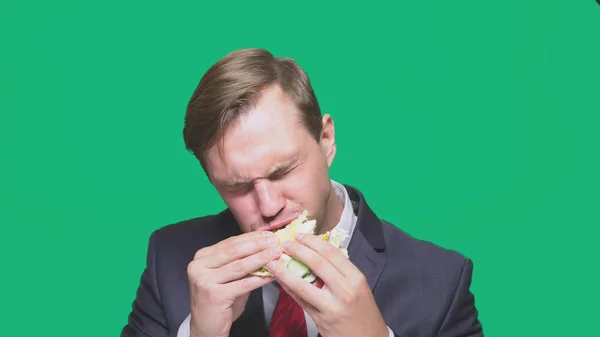 Businessman eating a sandwich on a green background. quick lunch concept — Stock Photo, Image