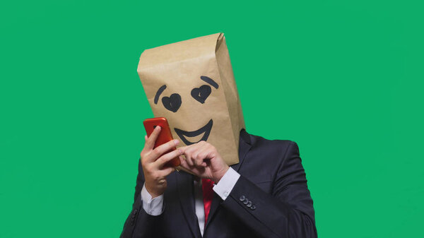 концепция эмоций, жестов. человек с бумажными пакетами на голове, с раскрашенным смайликом, улыбкой, радостью, любовью. разговор по мобильному телефону
