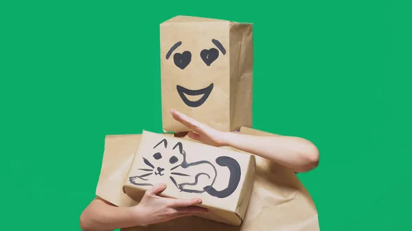 Concepto de emociones, gestos. un hombre con un paquete en la cabeza, con un emoticono pintado, sonrisa, ojos cariñosos. juega con un gato dibujado en la caja . — Foto de Stock