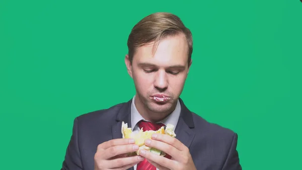 Empresário comendo uma sanduíche em um fundo verde. conceito de almoço rápido — Fotografia de Stock