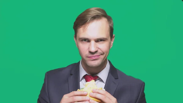 Empresário comendo uma sanduíche em um fundo verde. conceito de almoço rápido — Fotografia de Stock