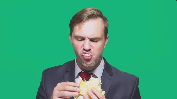 Empresário comendo uma sanduíche em um fundo verde. conceito de almoço rápido — Fotografia de Stock