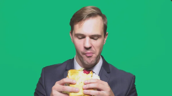 Hombre de negocios comiendo un sándwich sobre un fondo verde. concepto de almuerzo rápido — Foto de Stock