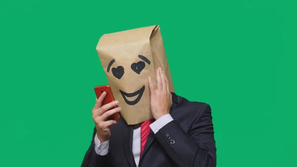 Concepto de emociones, gestos. un hombre con bolsas de papel en la cabeza, con un emoticono pintado, sonrisa, alegría, amor. hablando por un teléfono celular —  Fotos de Stock