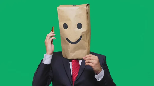 Begreppet känslor, gester. en man med papperspåsar på hans huvud, med en målad uttryckssymbol, leende, glädje. talar i en mobiltelefon — Stockfoto