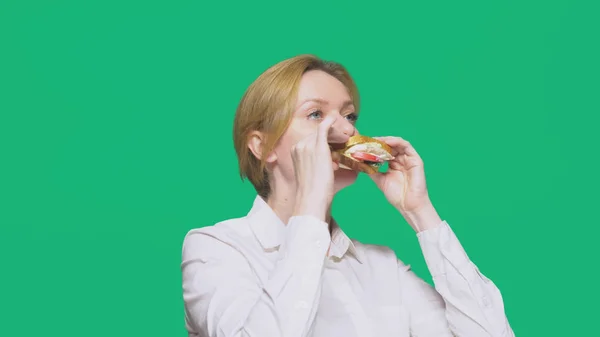 Zakenvrouw eten van een boterham op een groene achtergrond. snelle lunch concept. — Stockfoto