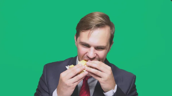 Empresário comendo uma sanduíche em um fundo verde. conceito de almoço rápido — Fotografia de Stock