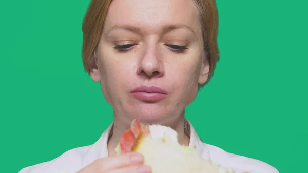 Mulher de negócios comendo uma sanduíche em um fundo verde. conceito de almoço rápido . — Fotografia de Stock