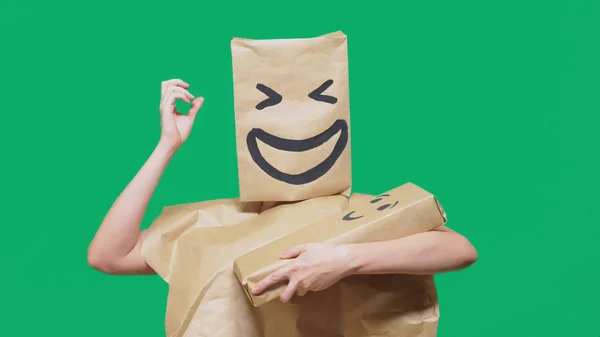 Concepto de emociones, gestos. hombre con un paquete en la cabeza, con un emoticono pintado, sonrisa, alegría, risa. juega con el niño pintado en la caja . — Foto de Stock