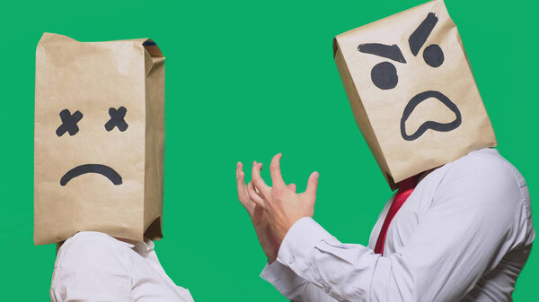 The concept of emotions and gestures. Two people in paper bags with smileys. Aggressive smiley swears. The second crying sad
