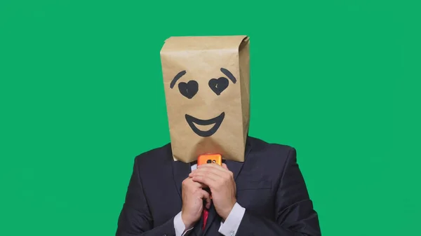 Concepto de emociones, gestos. un hombre con bolsas de papel en la cabeza, con un emoticono pintado, sonrisa, alegría, amor. hablando por un teléfono celular — Foto de Stock