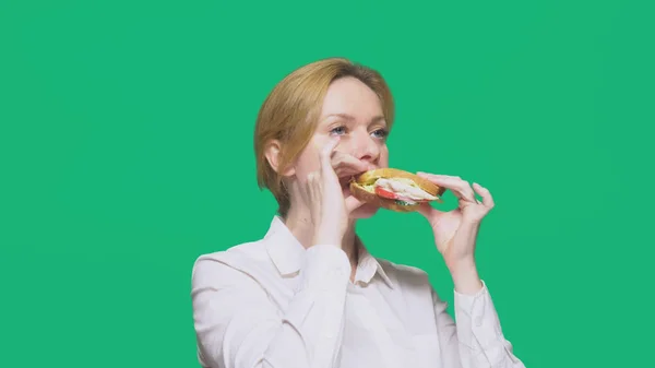 Donna d'affari mangiare un panino su uno sfondo verde. concetto di pranzo veloce . — Foto Stock