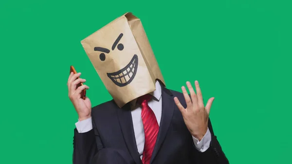 Begreppet känslor, gester. en man med ett paket på huvudet, med en målad svart smiley, en djävul, listig, göra, talar i en mobiltelefon. — Stockfoto
