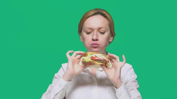 Business woman eating a sandwich on a green background. quick lunch concept. — Stock Photo, Image