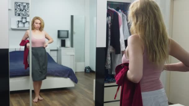 Odzież, szafa, moda, styl oraz koncepcja ludzi. zdziwiony Blondynka sprawia, że wybór ubrań, stojąc koło szafy i patrząc na siebie w lustrze — Wideo stockowe