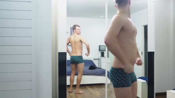 Молодий чоловік перевіряє свої м'язи перед дзеркалом у спальні — стокове відео