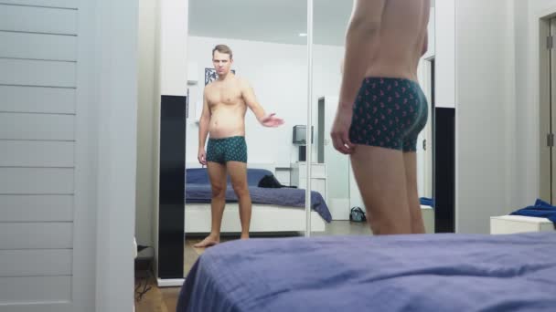 Молодий чоловік перевіряє свої м'язи перед дзеркалом у спальні — стокове відео