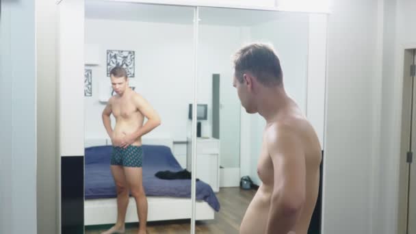 Junger Mann überprüft seine Muskeln vor einem Spiegel im Schlafzimmer — Stockvideo