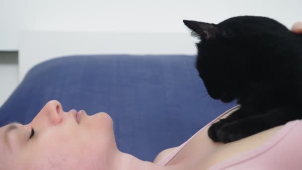 女孩与猫。美丽的金发碧眼的女孩躺在床上, 爱抚她的黑猫。照顾动物。对宠物的爱 — 图库视频影像