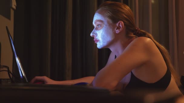 jeune femme avec masque cosmétique sur le visage travaillant avec ordinateur portable à la maison le soir. naturel 