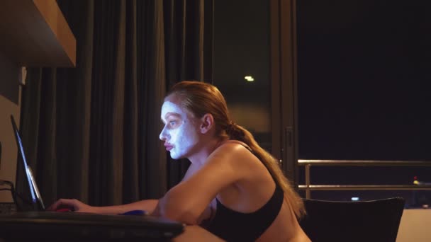 Junge Frau mit Kosmetikmaske im Gesicht, die abends zu Hause mit Laptop arbeitet. Natürlichkeit — Stockvideo