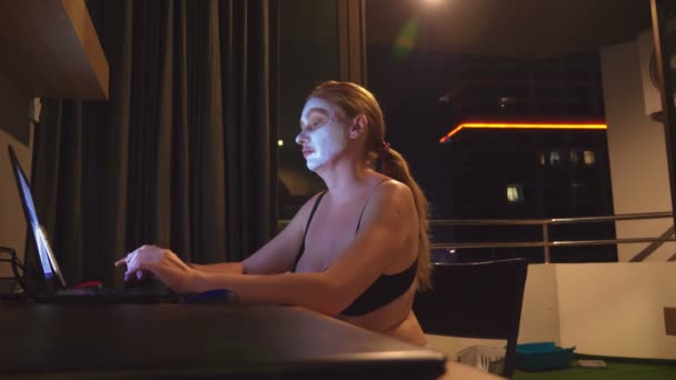 Young woman with cosmetic mask on face working with laptop at home in the evening. naturalness — Stock Video