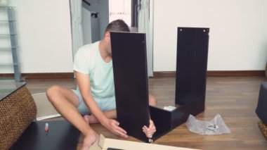 Genç bir adam bağımsız olarak mobilya evinin oturma odasında toplar. Bir adam bilgisayar masası toplar.