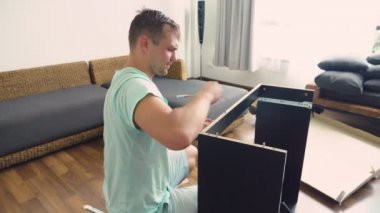 Genç bir adam bağımsız olarak mobilya evinin oturma odasında toplar. Bir adam bilgisayar masası toplar.