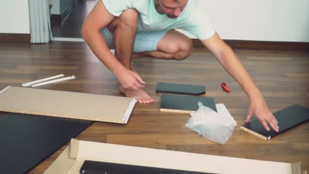 Un jeune homme recueille indépendamment des meubles dans le salon de sa maison. Un homme recueille un bureau d'ordinateur . — Video