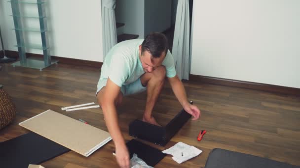 Een jonge man verzamelt zelfstandig meubels in de woonkamer van zijn huis. Een man verzamelt een computerbureau. — Stockvideo