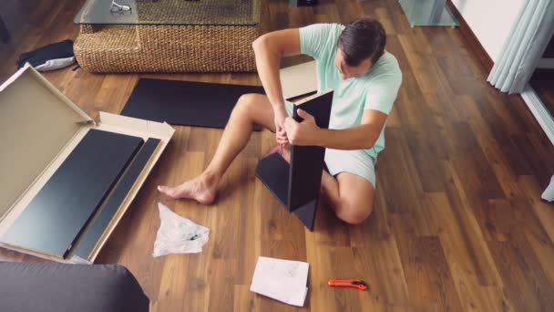 Młody człowiek zbiera niezależnie meble w salonie swojego domu. Człowiek zbiera biurko komputerowe. — Wideo stockowe