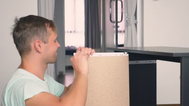 A young man independently collects furniture in the living room of his house. A man collects a computer desk. — Stock Video